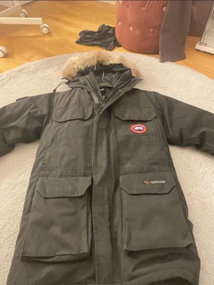 Canada Goose - ÄKTA. Säljer en svart dunparkas från Canada Goose med klassisk patch på bröstet och stor huva med äkta päls. Jackan har flera stora fickor, dragkedja och kardborreknäppning framtill. Perfekt för kalla vinterdagar och riktigt snygg streetstil. den har varit inne på kemtvätt.  Priset går absolut att diskutera 
