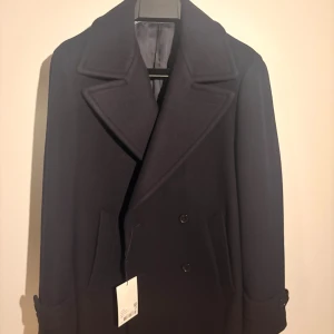  skepparkavaj i ull från Suitsupply - Elegant skepparkavaj i marinblå ullblandning från Suitsupply. Klassiskt, höftlångt snitt med lätt vadderade axlar, dubbelknäppt stängning och passpoalfickor. Stormflik och enkelsprund ger både stil och funktion under vintern.  Rocken är helt ny, aldrig använd och har kvar originaletiketter. Nypris: 4 699 kr Mitt pris: 3699 kr  Storlek: 44 (Slim fit) Passar dig som vill ha en skräddad men ledig siluett