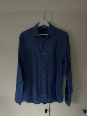 Riley linneskjorta blå - Blå ursnygg populär och trendig Riley linne skjorta i storlek M. Superfint skick då den är använd mycket sparsamt och perfekt till alla möjliga tillfällen! Inga defekter, pris ej hugget i sten och tveka inte vid minsta fråga eller fundering!