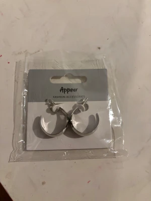 Silvriga chunky hoops från Appear - Snygga silvriga örhängen i chunky hoop-modell från Appear. De är halvrunda och har en blank metallfinish som ger en cool och modern vibe. Perfekta för att lyfta vilken outfit som helst med lite extra edge.