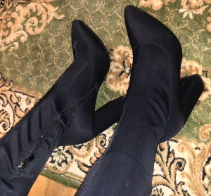 Svarta stövletter med klack - Säljer ett par svarta stövletter med spetsig tå och hög klack. Skorna har en snygg, strömlinjeformad design med dragkedja på sidan för enkel på- och avtagning. Materialet är stretchigt syntet som sitter tight runt benet och ger en cool siluett.