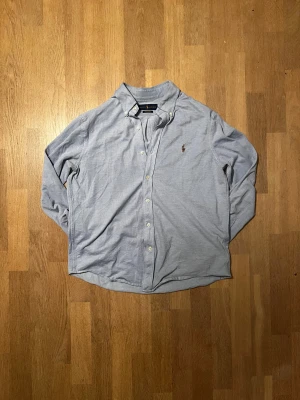 Ljusblå skjorta från Ralph Lauren - Klassisk ljusblå skjorta från Ralph Lauren med broderad logga på bröstet. Skjortan har lång ärm, knappar framtill och en avslappnad passform. Tillverkad i mjuk bomull, perfekt för en clean och stilren look. ✅   Passar för runt 184 🙌  9.5/10 skick  ✅ Skickar inom 48 timmar om inte samma dag 🚚Nypris cirka 1800