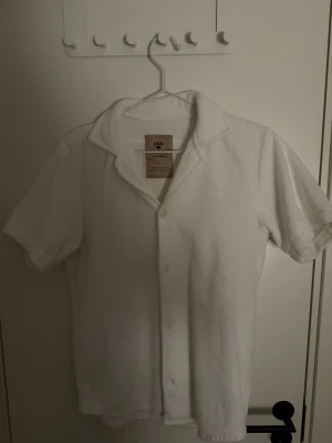 Vit frottéskjorta från OAS, S - Fräsch vit skjorta från OAS i mjuk frotté, perfekt att dra på sig efter badet. Skjortan har korta ärmar, klassisk krage och knäppning framtill. Tillverkad i 100% bomullsfrotté, designad i Sverige och gjord i Portugal. Enkel och clean stil för chill dagar.