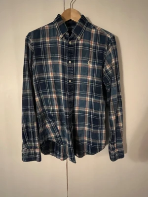 Blå rutig skjorta från Ralph Lauren - Snygg blå rutig skjorta från Ralph Lauren i klassisk passform. Skjortan har långa ärmar, knappar framtill och en liten broderad logga på bröstet. Tillverkad i mjuk bomull som känns skön mot huden. Perfekt för dig som gillar en chill och stilren look.                                                                Hör gärna av dig om minsta lilla fundering.