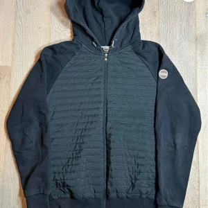 Svart hoodie från Colmar med quiltad front - Svart hoodie från Colmar med quiltad front och rygg, hel dragkedja och huva. Detta är en förbeställning och snabbast frakt är 3 dagar. Tröjan har långa ärmar och en liten Colmar-logga på ena ärmen. Mycket bra skick utan hål. Perfekt för kyliga dagar och snygg till jeans eller joggers. Pris kan alltid diskuteras. Skriv om frågor uppstår. 