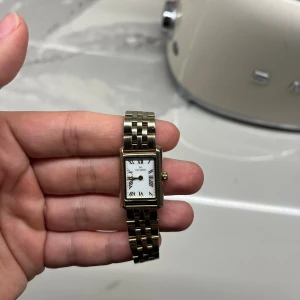 Guldig rektangulär klocka från Mockberg - Stilren klocka från Mockberg med rektangulärt ur i vitt och romerska siffror. Armbandet är i guldtonad metall med klassisk länkdesign. Perfekt accessoar för dig som gillar en tidlös och elegant look.