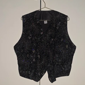 Vintage glittrig kostymväst - 🌷FÖRST TILL KVARN!🌷Vintage svart kostymväst med glittrigt mönster. Den glittrar sååå mycket och är en festlig nice touch under en svart kavaj eller tuxedo. Köpte den secondhand så vet inte om den är manlig eller kvinnlig men tycker att både & skulle passa snyggt i denna. Strl L men kan föminskas en aning i midjan bakifrån så den skulle kunna passa m (jag) & s lite oversized. Handtvätt endast!. VILL BLI AV MED ASAP!
