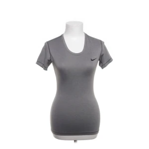 Grå Nike Dri-Fit t-shirt, tight passform - Snygg grå t-shirt från Nike med Dri-Fit-teknologi som håller dig torr under träningen. Modellen har korta ärmar, rund halsringning och en tight passform. Diskret Nike-logga på bröstet. Perfekt för gymmet eller sportaktiviteter.