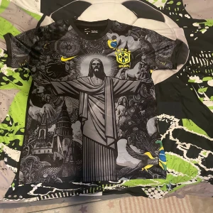 Nike Brasil Dri-Fit fotbollströja M - Unik svart och grå Brasilien fotbollströja från Nike med Dri-Fit-material. Framsidan har ett stort tryck av Kristusstatyn och detaljerade illustrationer, samt gula Brasil-loggor och Nike swoosh. Korta ärmar med grafiskt mönster och rund hals.