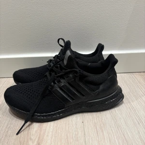 Svarta Adidas Ultraboost sneakers - Säljer ett par helsvarta Adidas Ultraboost sneakers med stickad ovandel, snörning och platt sula. Skorna har en sportig vibe med diskreta detaljer och Boost-mellansula för extra komfort. Perfekta för dig som gillar stilrena och bekväma sneakers.kom dm för frågor🧐, vill sälja så snabbt som möjligt så pris kan diskuteras snabbt och smidigt. 