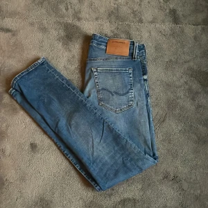 Slim Glenn jeans från Jack & Jones - Snygga blå jeans från Jack & Jones i modellen Slim Glenn. Jeansen har en slim passform, klassisk femficksdesign och coola slitningar framtill. Perfekta för dig som gillar en smalare siluett och vill ha ett par stilrena jeans i garderoben.