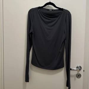 Mörk grå långärmad topp från BikBok - En mörkgrå  långärmad topp från BikBok med enkel och stilren design. Toppen har en något lös passform och är tillverkad i ett mjukt, stretchigt syntetmaterial. Perfekt att matcha med jeans eller kjol för en clean look. Säljer likadan o svart 