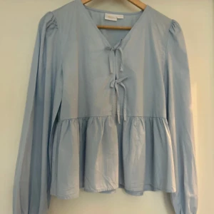 Ljusblå blus  - Supersöt ljusblå blus med v-ringning och två rosetter framtill. Tyvärr har den inte kommit till användning hos mig och hoppas någon annan kan få bättre användning för den fina tröjan💘