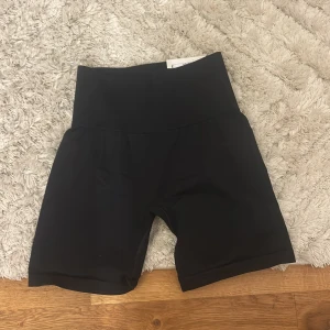 Svarta biker shorts från H&M Move - Svarta biker shorts från H&M Move med hög midja och tight passform. Perfekta för träning eller när du vill ha en sportig look. Tillverkade i stretchigt syntetmaterial som sitter skönt och följer kroppen.
