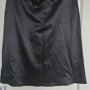 Svart siden  kjol från Stories, M - Snygg svart långkjol från Stories i storlek M. Kjolen har en klassisk A-linjeform och är tillverkad i ett slätt, lätt glansigt material som ger en stilren look. Perfekt för dig som gillar minimalistisk stil och vill ha en enkel men elegant kjol. Dragkedja I sidan resår i midjan använd 1 gång 