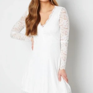 Vit spetsklänning med v-ringning - Superfin vit klänning med v-ringning och långa ärmar i spets. Klänningen har en figurnära överdel och lätt utställd kjol. Spetsen ger en romantisk känsla och de genombrutna ärmarna gör den extra snygg. Perfekt för dig som vill sticka ut med en elegant look.