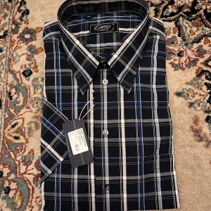 Rutig skjorta från Oscar of Sweden - Snygg rutig skjorta från Oscar of Sweden i mörkblått, vitt och grått. Skjortan har klassisk krage, knäppning framtill och är tillverkad i 100% bomull. Perfekt för dig som gillar stilrena och tidlösa mönster.