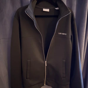 Les duex tröja  - Snygg svart ziptröja från Les Deux med stilren design och diskret logga på bröstet. Tröjan har hel dragkedja, ståkrage och två fickor framtill. Perfekt för lager-på-lager och passar till det mesta. Materialet är mjukt och skönt mot huden.