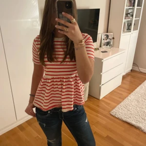 Randig peplumtop från Zara - Superfin peplumtop från Zara i vitt och rött med horisontella ränder. Toppen har korta ärmar, rund halsringning och en volangig peplum nedtill som ger en söt och avslappnad look. Perfekt att styla med jeans eller kjol för en trendig vibe. Skriv om ni har frågor eller vill köpa🙏💕
