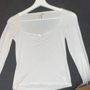 Långärmad vit tröja med rosett  - En jättefin långärmad lite magtröja från Nelly som använts 4 ggr. kan använda vardagligt men även uppklätt, säljer för att den inte passar längre. Orginal pris 300kr. Pris kan diskuteras❤️
