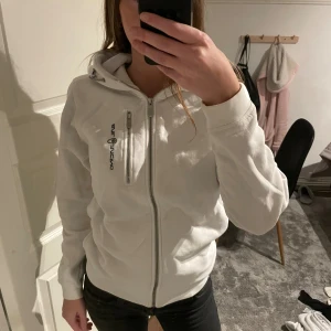 Vit hoodie med dragkedja från Sail Racing - Säljer en vit hoodie med dragkedja från Sail Racing med huva och två dragkedjor framtill 