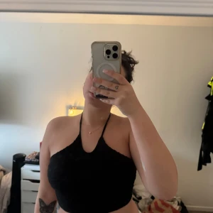 Svart halterneck topp från SHEIN - Säljer en svart halterneck topp från SHEIN i storlek M. Toppen har en croppad passform och är tillverkad i ett vågigt, ribbat tyg med knyt runt nacken. Perfekt för dig som gillar stilrena och trendiga plagg med lite edge.