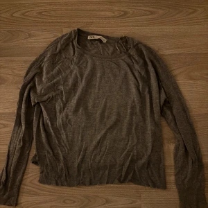Grå långärmad tröja från Zara - En enkel och stilren grå långärmad tröja från Zara. Tröjan har rund halsringning och ribbade muddar vid ärmslut och nederkant. Perfekt för lager-på-lager och passar till allt. Mjuk och tunn i materialet, vilket gör den skön att bära.