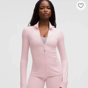 Lululemon rosa zip-tröja - Snygg ljusrosa zip-tröja från Lululemon med figurnära passform och hög krage. Tröjan har långa ärmar med tumhål, praktiska fickor med dragkedja och diskret logga på ryggen. Perfekt för träning eller chill. Materialet är mjukt och stretchigt, troligen polyester.
