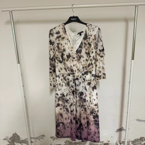 Blommig långklänning från Esprit - Säljer en superfin långklänning från Esprit med blommigt mönster i beige, svart och lila toner. Klänningen har v-ringning, trekvartsärm och ett band i midjan för snygg passform. Materialet är mjukt och lätt polyester, perfekt för vår och sommar.