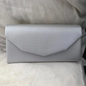 Silver kuvertväska med kedja - Fin silverfärgad kuvertväska med kedjerem, som går o lägga i väskan så man har en handväska oxå, kjedhan går även att ta av om man vill oxå. Väskan stängs med magnetlås. Använd en gång, men dedär på sidan inuti ”locket” kom när jag köpte väskan men syns inte när väskan är stängd