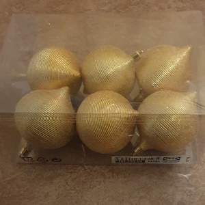 Julkulor - Bilderna visar en förpackning med sex gyllene julgranskulor från IKEA. Kulorna har en unik, ribbad yta och spetsig form, och levereras i originalförpackning. Dom är perfekta för att dekorera granen med elegant glans.