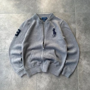 Polo Ralph Lauren - Snygg grå stickad tröja från Polo Ralph Lauren. Tröjan har dragkedja framtill. Storleken är egentligen XL men den passar som en herr S. Perfekt för dig som letar efter något att ha under vinterjackan! Om du är intresserad är det bara att skicka meddelande! MVH Olle. (Pris kan diskuteras)