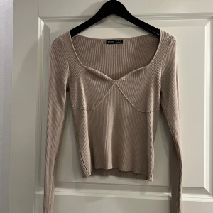 Beige ribbad topp från SHEIN - Säljer en beige ribbad topp från SHEIN i storlek S. Toppen har lång ärm, croppad passform och snygg v-ringad hals med markerade sömmar framtill. Materialet är mjukt och stretchigt, perfekt för att styla med jeans eller kjol. Toppen är helt oanvänd 