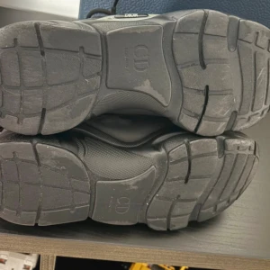 Svarta Dior sneakers med snörning - Säljer ett par svarta Dior sneakers med chunky platt sula och snörning. Skorna har mesh och skinnpaneler, samt reflekterande detaljer på hälen. Innersulan är märkt med Dior-loggan och de levereras med originalkartong och dustbag.