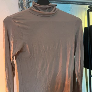 Beige polotröja i mjuk bomull - Säljer en stilren beige polotröja med lång ärm och hög krage. Tröjan är i mjuk och tunn bomull, perfekt att ha som lager eller för en clean look. Enkel att matcha med både jeans och kjol.