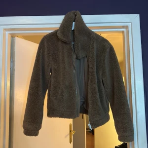 Brun teddyjacka från H&M Divided - Mysig brun teddyjacka från H&M Divided i storlek S. Jackan har en hög krage, dragkedja framtill och är helfodrad med slät insida.