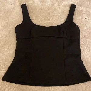 Svart korsett-topp med rosett - Snygg svart korsett-topp med breda axelband och en stor rosett framtill som ger en extra cool touch. Den är Xs men skulle mer säga att den sitter som S. Toppen har en figurnära passform och är tillverkad i ett slätt, lite stadigt material. Dragkedja i sidan för enkel på- och avtagning. Perfekt för dig som gillar stilrena detaljer.