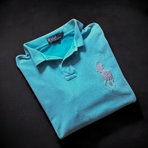 Turkos Polo Ralph Lauren piké L - Turkos pikétröja från Polo Ralph Lauren i storlek L, custom fit. Klassisk krage, korta ärmar och knappar framtill. Stor broderad polospelare på bröstet och siffror på ena ärmen. Tillverkad i mjuk bomull som är skön mot huden. Rökfritt hus. Skick 7/10. Nypris 1995kr. Mitt pris 147,65kr