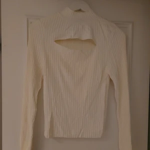 Vit ribbad polotopp från Gina Tricot - Säljer en vit ribbad polotopp från Gina Tricot i storlek M. Toppen har lång ärm, hög krage och en snygg öppen ryggdetalj. Materialet är mjukt och stretchigt, perfekt för dig som gillar stilrena och trendiga plagg med en twist.