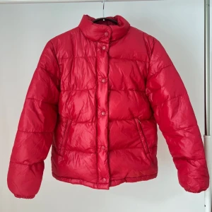 Dunjacka <3 - Röd dunjacka från Amica. Jackan har en hög krage och stängs med knappar. Den har även fickor på sidorna. Storlek 36 <3