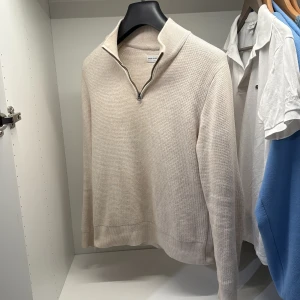 Beige stickad half zip från These Glory Days - Snygg beige stickad tröja från These Glory Days i storlek S. Tröjan har en stilren half zip-dragkedja och ribbade muddar vid ärmslut och nederkant. Perfekt för lager-på-lager och chill stil under höst och vinter.