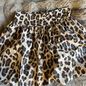 Leopardmönstrad kjol från Kappahl - Snygg kortkjol från Kappahl med leopardmönster i beige och svart. Kjolen har en bred linning och är tillverkad i mjuk bomull som gör den bekväm att bära. Säljer då den är för liten för mig, storlek 164