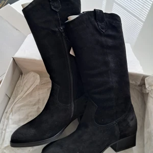 Svarta mockastövlar från Tamaris - Snygga svarta stövlar från Tamaris i mjuk mocka med låg klack och dragkedja på sidan. Klassisk design med rund tå och diskreta sömdetaljer. Perfekta till höst- och vinterlooken, passar till både jeans och kjol.