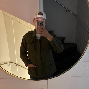 Olivgrön utility field jacka - Olivgrön utility-inspirerad jacka med fyra stora fickor framtill, axelklaffar och knäppning vid ärmslut. Jackan har en rak passform och är tillverkad i ett slitstarkt bomullstyg. Perfekt för lager-på-lager och en clean streetstyle-look. Pris kan diskuteras passar nog även Stor S