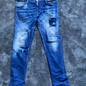 Blå slim jeans från Dsquared2 - Säljer ett par blå slim jeans från Dsquared2 med slitna detaljer och patch baktill. Jeansen har klassisk femficksdesign, låg midja och är tillverkade i jeansmaterial. Snyggt tvättade med coola slitningar för en trendig look.