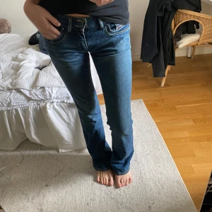 Blå jeans från Diesel, storlek 28 - Säljer ett par klassiska blå jeans från Diesel med snygg tvätt och raka ben. Jeansen har låg midja, fem fickor och coola detaljer vid fickorna. Tillverkade i Italien i slitstarkt bomullsjeans. Innerbenslängden är 86cm och jag är 175cm. Hör av er vid intresse eller frågor!