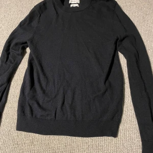 Svart merinoullströja These Glory Days - Klassisk svart rundhalsad tröja från These Glory Days i mjuk och lyxig merinoull. Långärmad modell med ribbade muddar och enkel, stilren design som funkar till allt. Perfekt för lager-på-lager under kyliga dagar. Pris kan diskuteras. Hör av er vid eventuella frågor