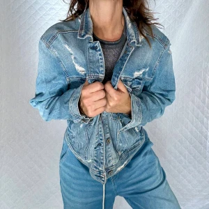 Oversized jeansjacka med tryck stl.L American Eagle - Snygg ljusblå jeansjacka med slitna detaljer och coolt tryck på ryggen: 'Coast to Coast Tour, SF LA Summer of 1977 BK NY'. Jackan har knappar framtill, bröstfickor med lock och en loose passform. Perfekt för dig som gillar streetstyle och vintagevibbar.