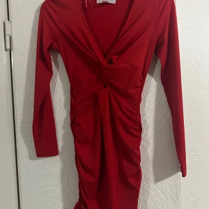 Röd omlottklänning från Amisu - Snygg röd kortklänning från Amisu med lång ärm och v-ringad omlottfront. Klänningen har twistad detalj framtill och rynkade sidor som ger en smickrande passform. Perfekt för dig som vill sticka ut med en färgstark look.