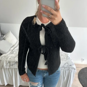 Svart stickad kofta med knyt - Svart stickad kofta med två knytband framtill. Koftan har lång ärm och en rak pass form. Super fin, varm och ferfekt till hösten. Antingen knyter man båda rosetterna eller bara nedersta (bild 2) använd väldigt fåtal gånger. Från Veromoda och märket pieces! Köpt för 400kr.
